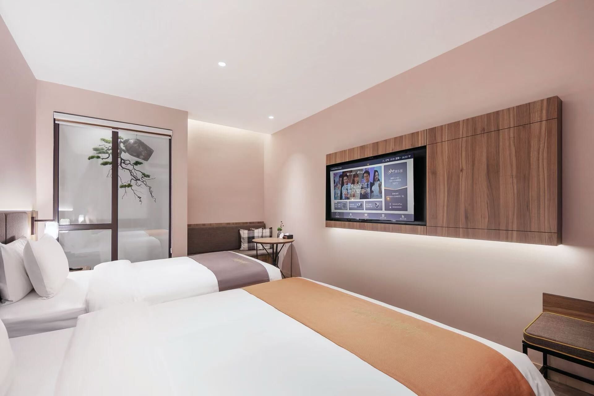 A modern hotel room with a large bed, a seating area with a small table, a TV mounted on the wall, and a decorative plant.