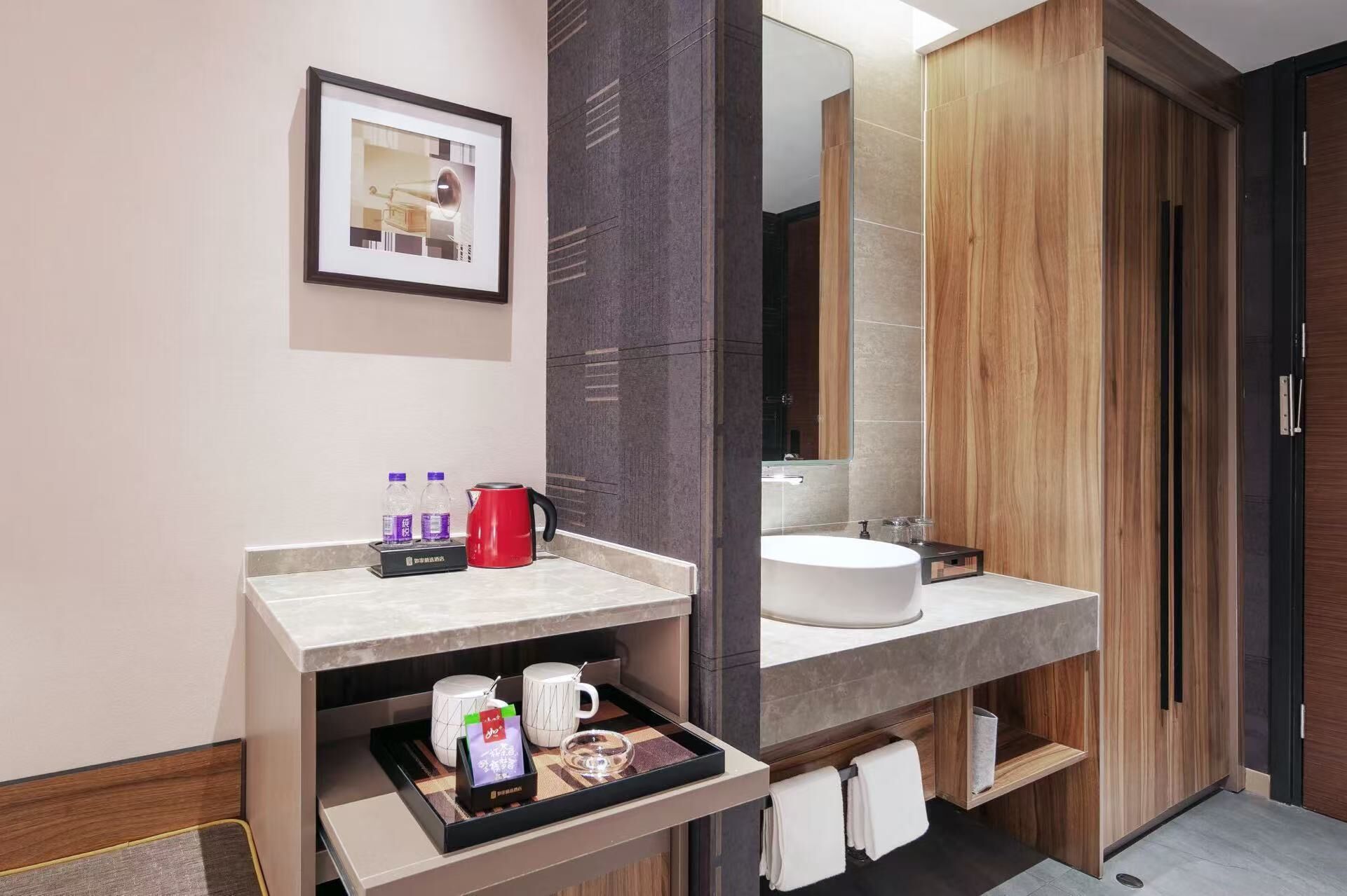 Une salle de bain moderne avec un grand miroir, un lavabo blanc, une bouilloire rouge et un plateau contenant des articles de toilette.
