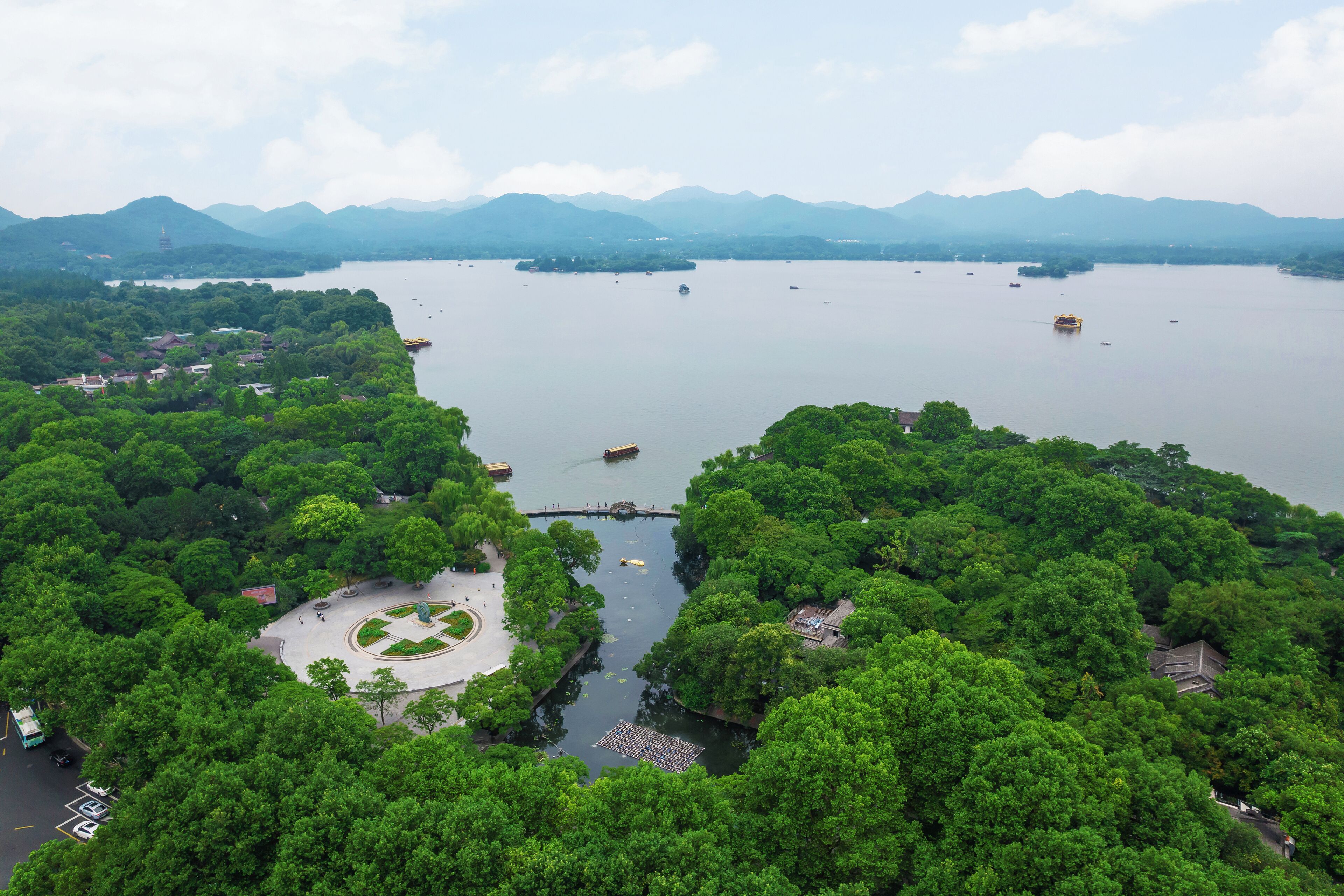 An aerial view of a park with a lake, surrounded by mountains and dense greenery.