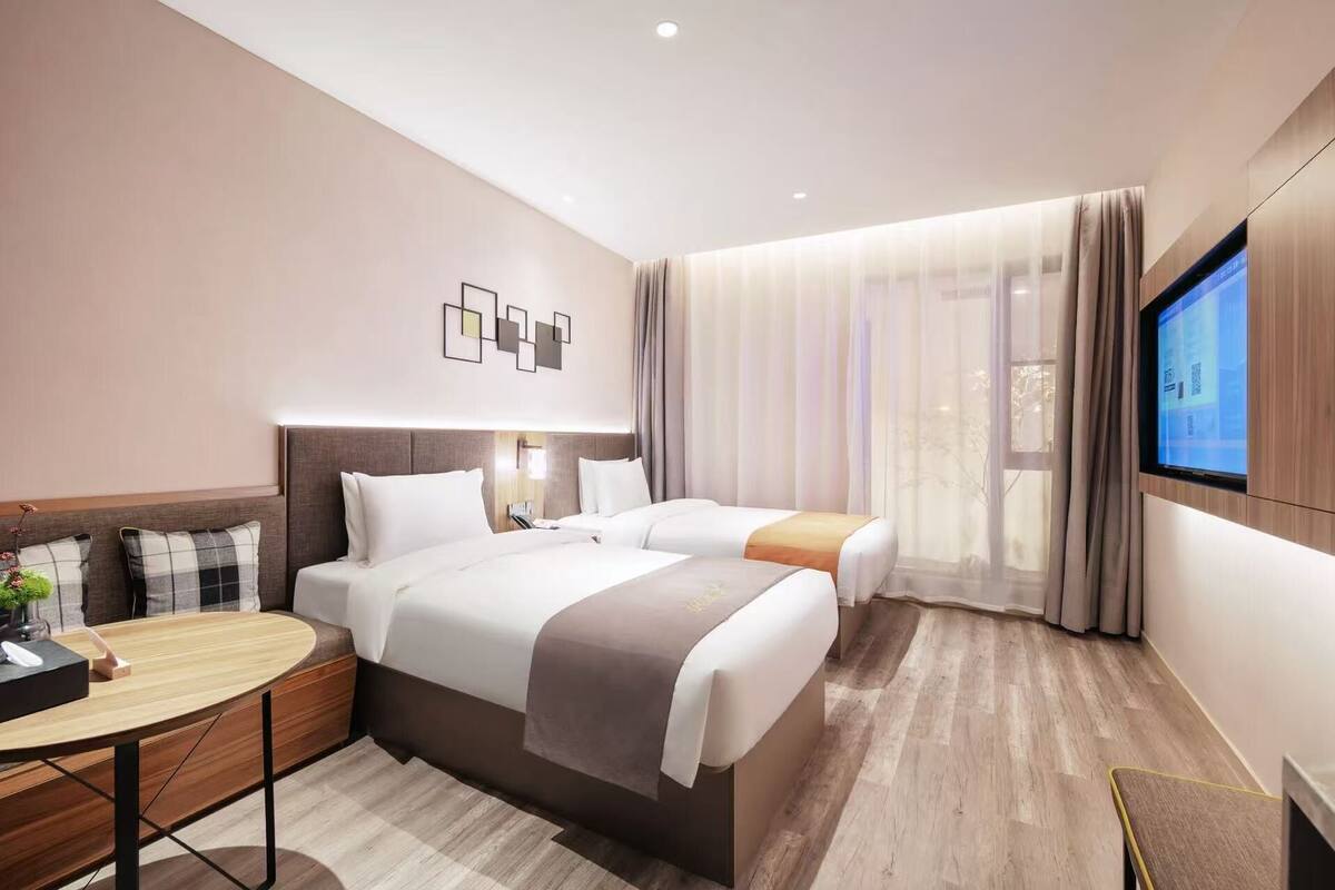 A hotel room with two beds, a desk, a TV, and a window with curtains.