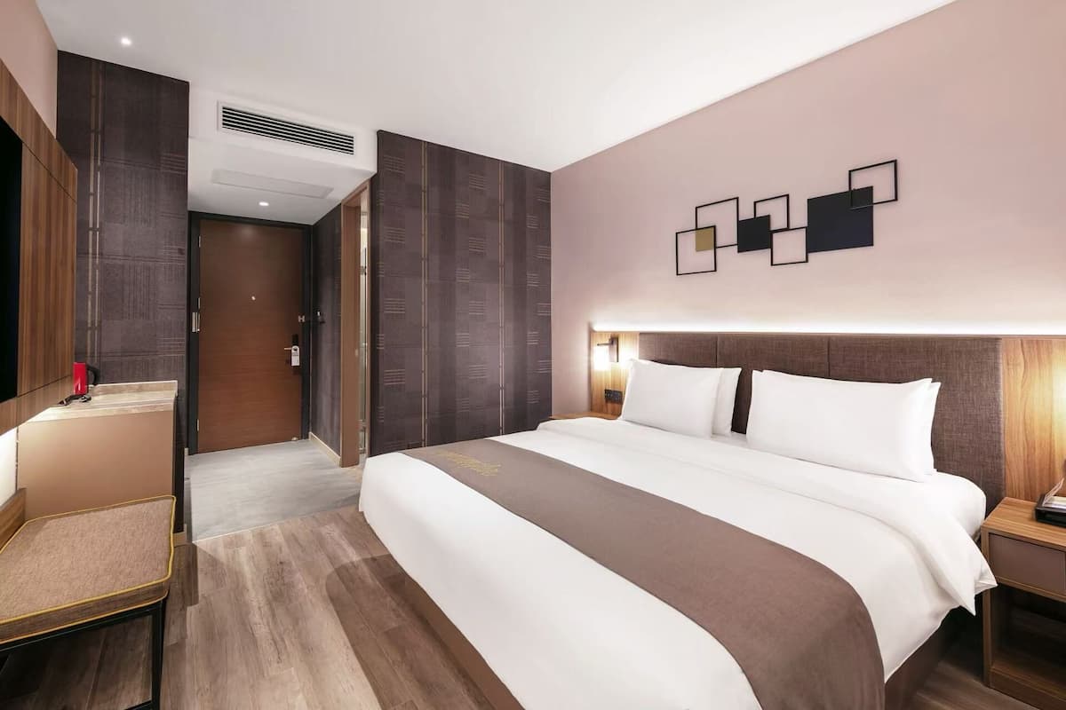 A hotel room with a large bed, a bedside table, a nightstand, a wardrobe, and a wall-mounted light fixture.