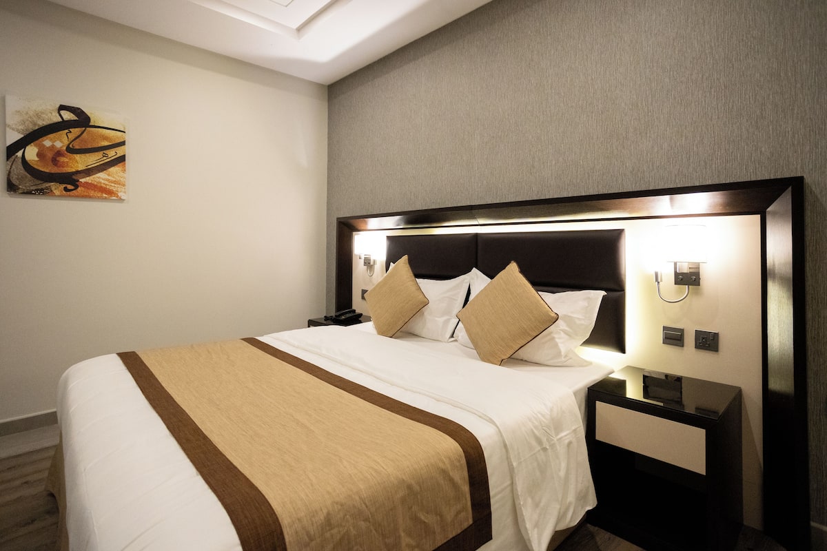 A neatly made bed with a headboard, a bedside table, and a wall-mounted lamp.