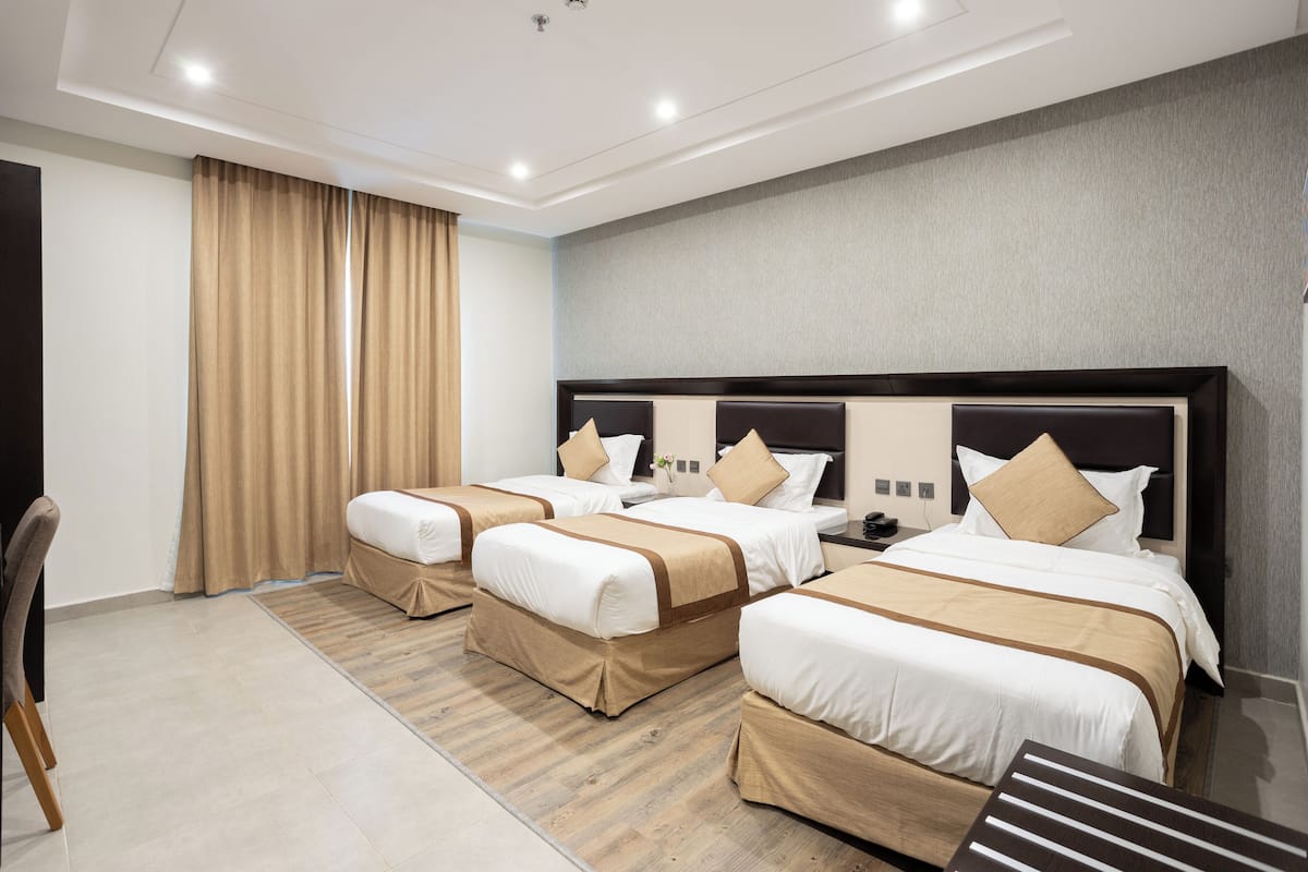 A hotel room with three beds, a desk, and a chair.