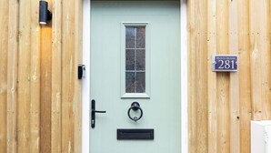 Uma porta verde clara com janela, campainha, caixa de correio e placa de número da casa.