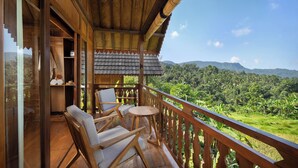 A wooden balcony with two chairs and a table, overlooking a lush green landscape with mountains in the distance. - Devani Resort Sidemen (Sidemen)