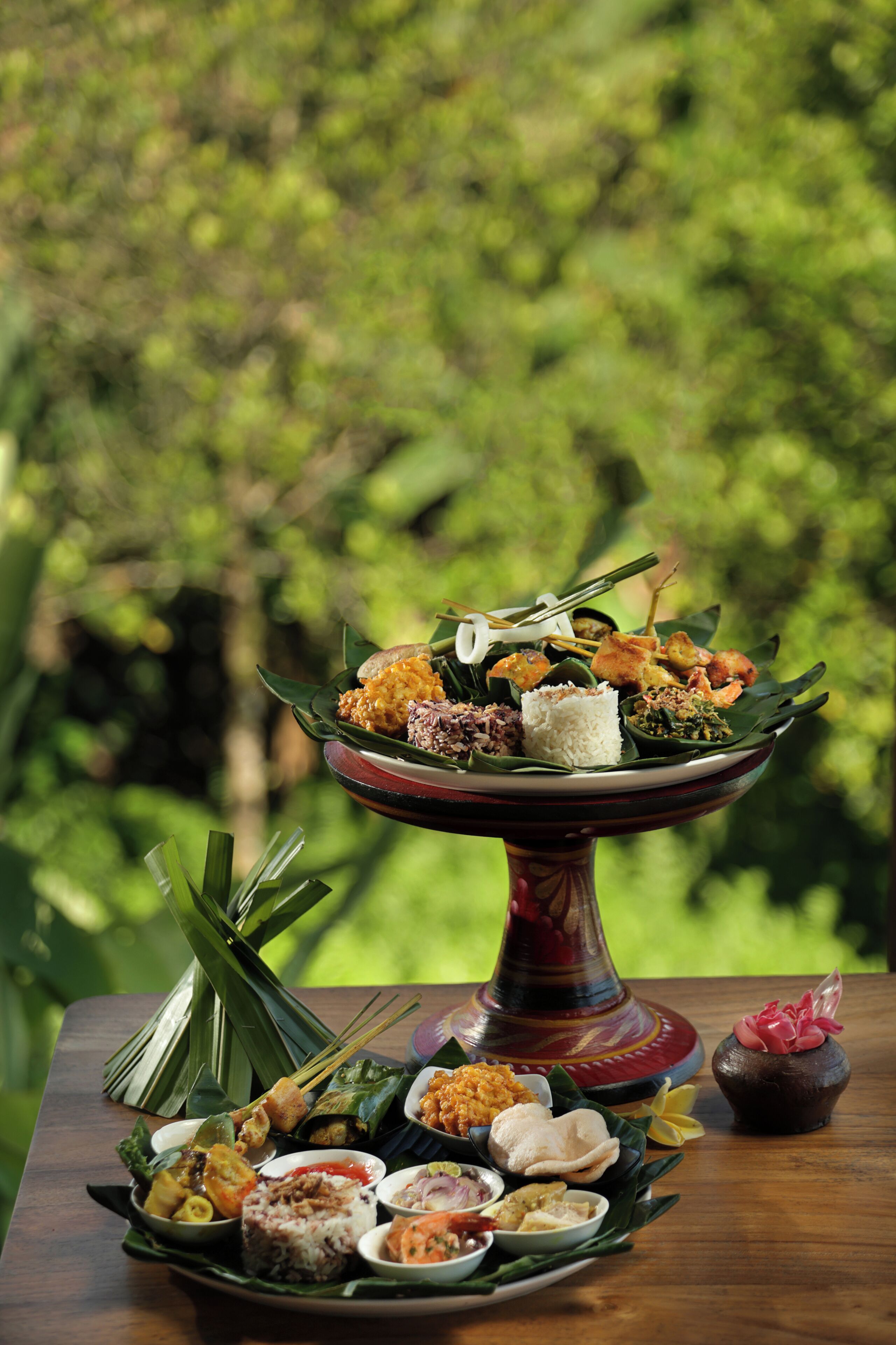 A variety of dishes arranged on a table with a wooden surface, set against a backdrop of greenery.