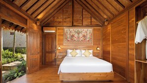 A wooden room with a bed, a nightstand, and a wall tapestry. - Devani Resort Sidemen (Sidemen)