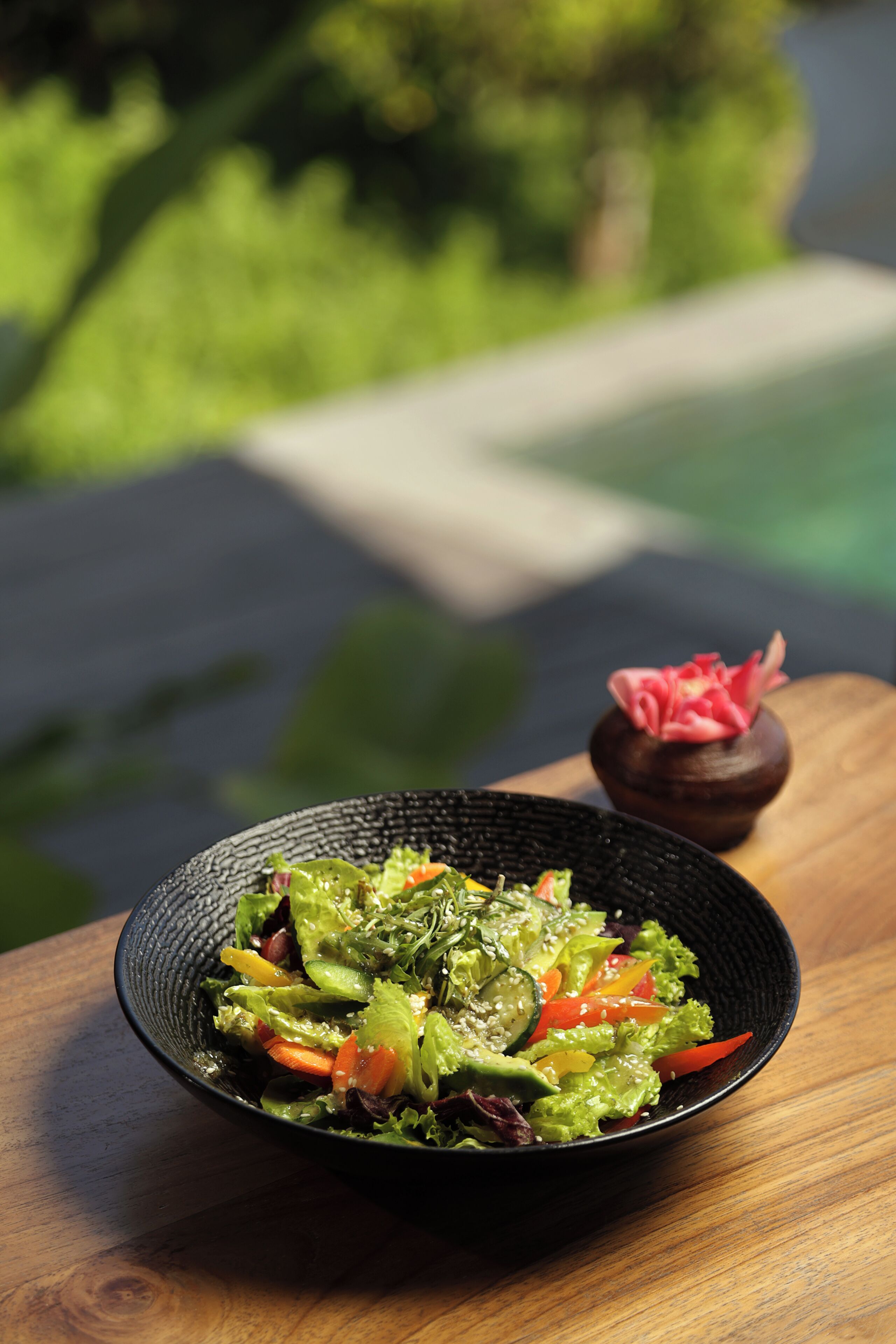 Een saladeschaal op een houten tafel, met een onscherpe achtergrond van buiten.