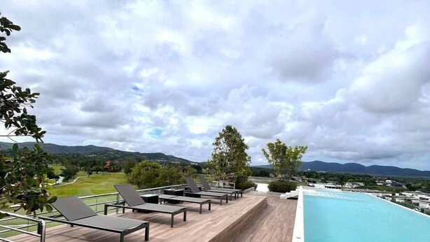 Ein Pool auf dem Dach mit Holzterrasse und Liegestühlen, mit Blick auf einen Golfplatz und Berge.