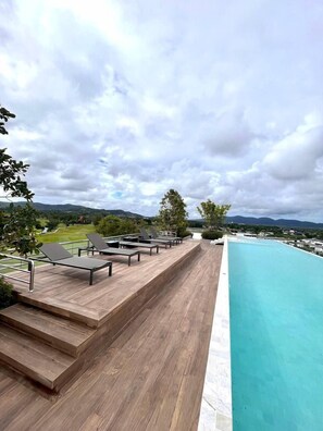 A rooftop pool with wooden deck and lounge chairs, overlooking a golf course and mountains. - Laguna SkyPark (Choeng Thale)