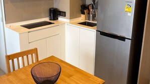 Eine kleine Küche mit Holzschränken, einem Edelstahlkühlschrank, einer Mikrowelle und einer Kaffeemaschine.