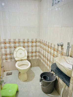 A small bathroom with a toilet, sink, and green stool. - Hotel Ashadeep (Ahmedabad)