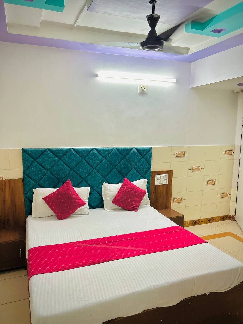 A neatly made bed with a teal headboard, white bedding, and a red throw blanket.