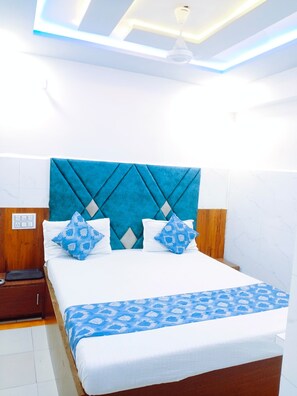 A neatly made bed with a patterned bedspread, a wooden headboard, and a nightstand with a lamp. - Hotel Ashadeep (Ahmedabad)