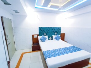 A hotel room with a bed, nightstand, and a door. - Hotel Ashadeep (Ahmedabad)
