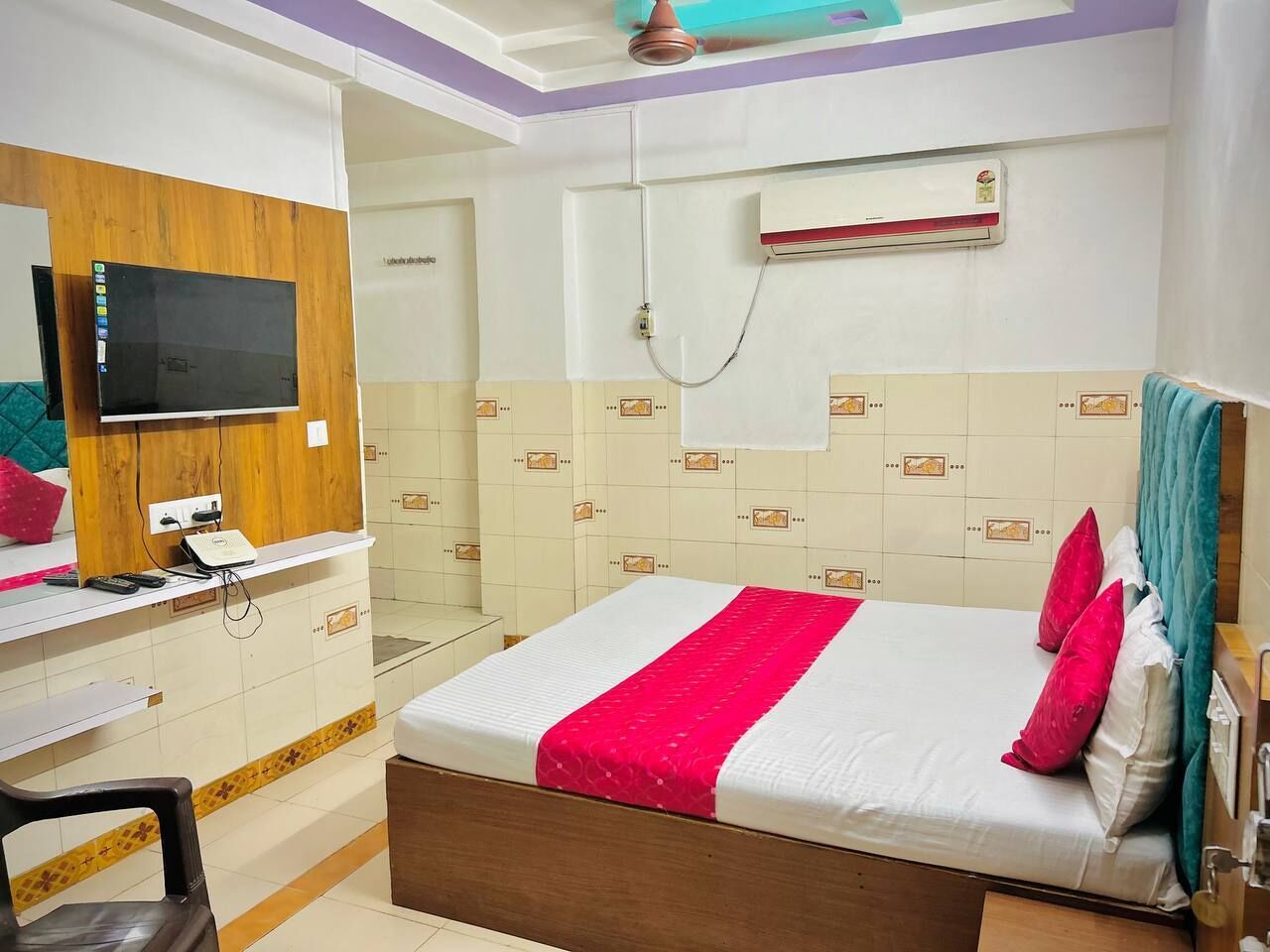 A hotel room with a bed, a desk, a mirror, an air conditioner, and a shower area.