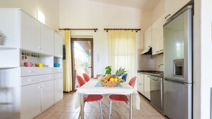 Una cocina con armarios blancos, un refrigerador de acero inoxidable y una mesa de comedor con sillas rojas.