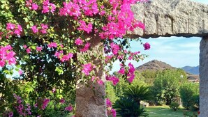 Un jardín con un arco de piedra, abundante vegetación y un cielo despejado.