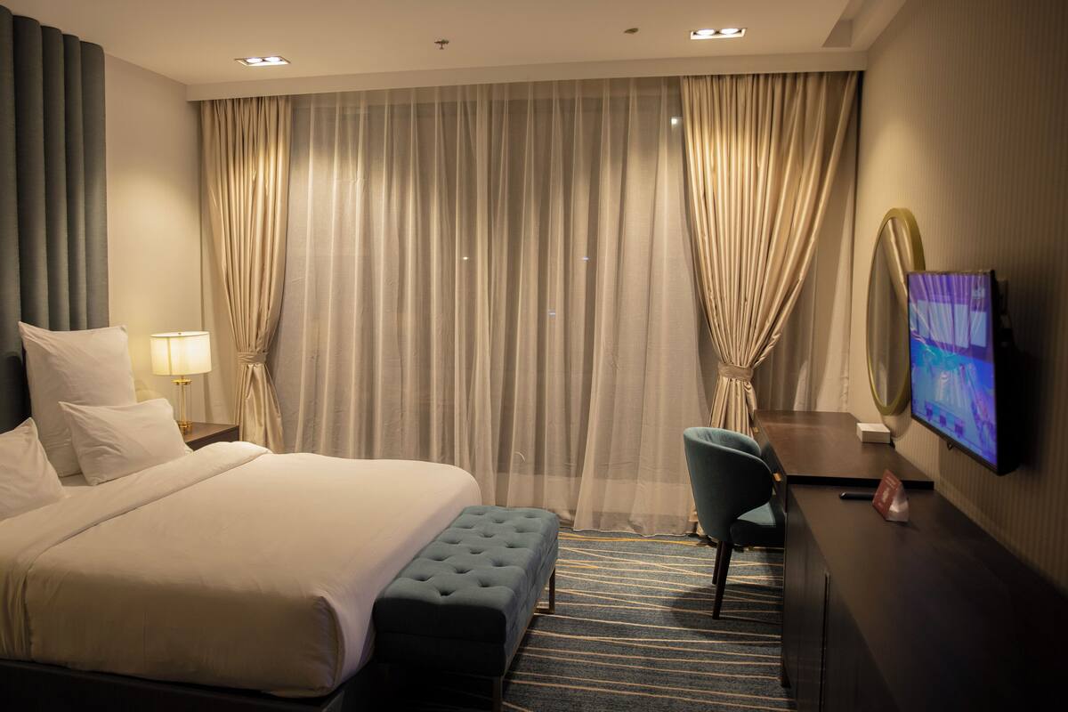 A hotel room with a large bed, a desk with a chair, a television, and curtains.
