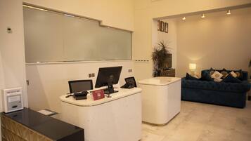 A reception desk with a computer, a phone, and a red box. There is a blue sofa and a lamp in the background.