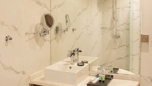 Un baño con pared de mármol, lavamanos integrado, espejo y ducha.