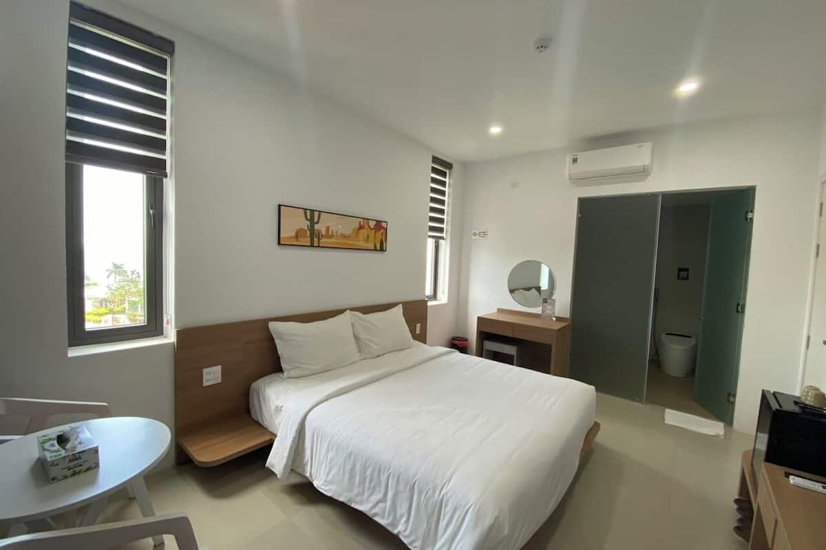 Ein modernes Hotelzimmer mit Bett, Nachttisch und kleinem Schreibtisch mit Stuhl.