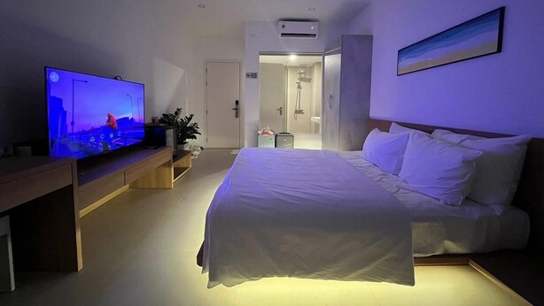 Una habitación de hotel moderna con una cama grande, un televisor de pantalla plana y un baño visible a través de una puerta abierta.
