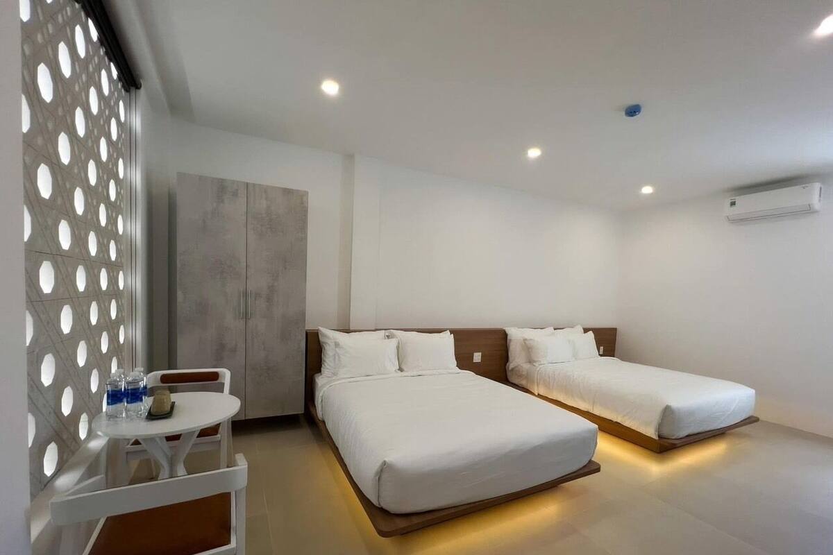 Ein modernes Hotelzimmer mit zwei Betten, einem kleinen Tisch mit Wasserflaschen und einer Wand-Klimaanlage.