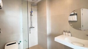 Un baño moderno con cabina de ducha de vidrio, un lavamanos blanco con espejo redondo y un inodoro.
