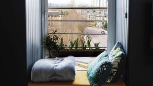 Un rincón acogedor para leer con asiento junto a la ventana, una lámpara y vistas de la ciudad.