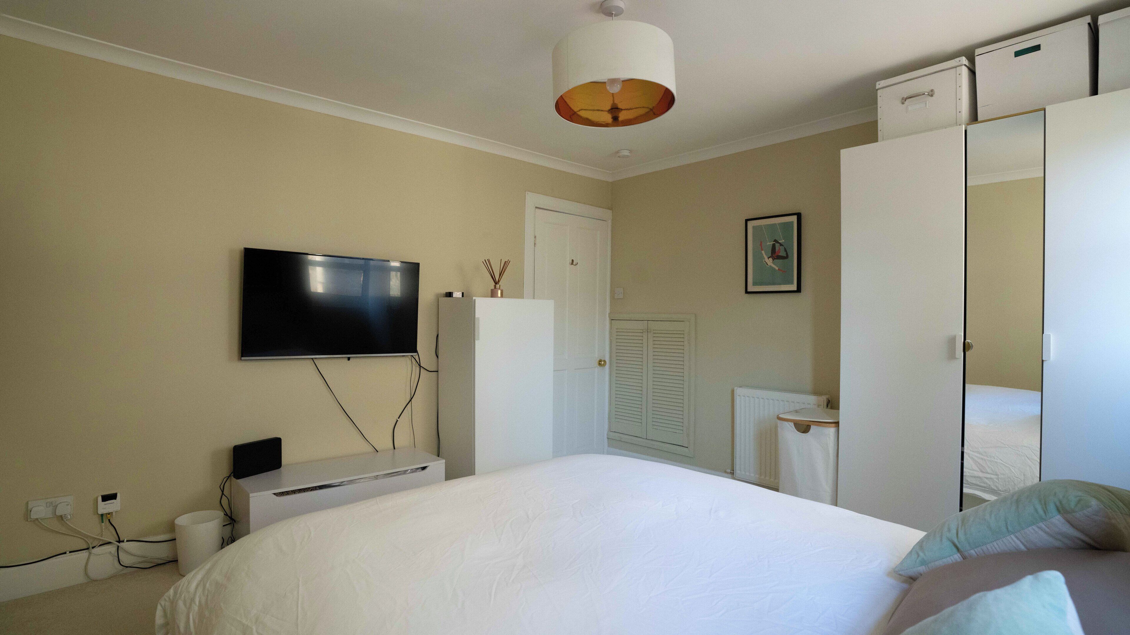 Un dormitorio con cama, televisor en la pared, armario y radiador.