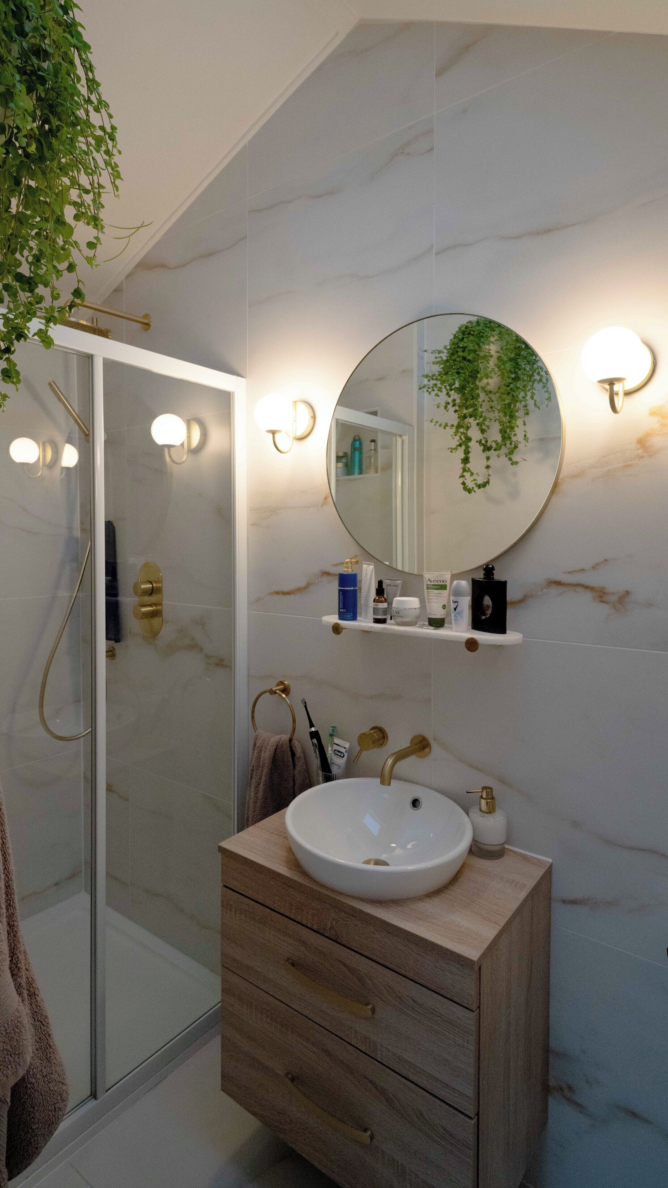 A bathroom with a glass-enclosed shower, a wooden vanity with a white sink, and a mirror with wall-mounted lights.