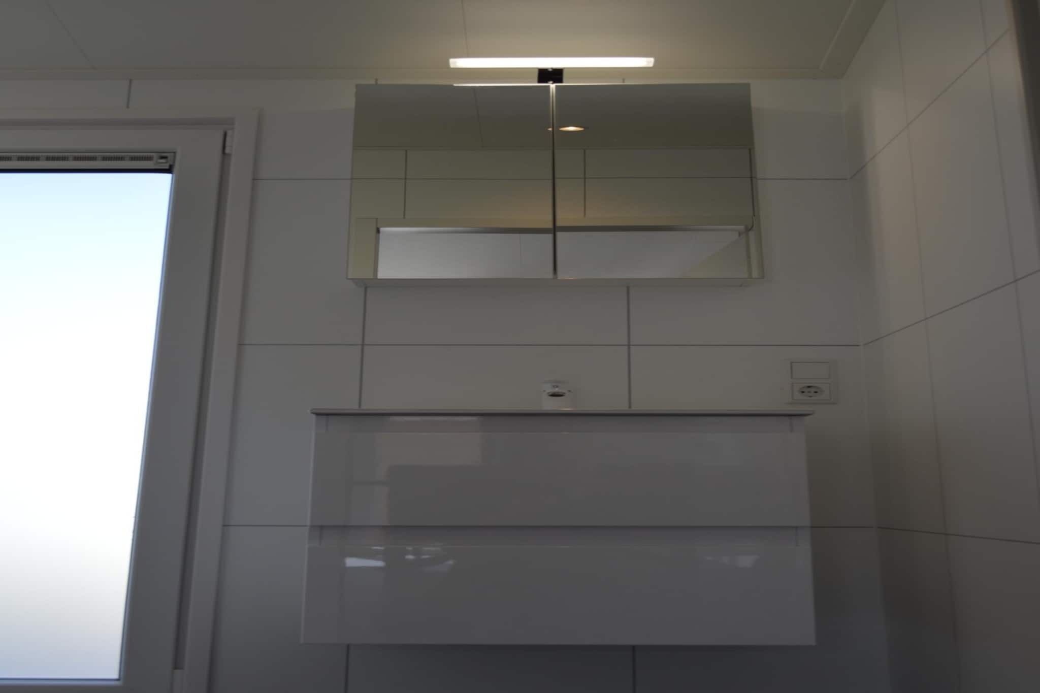 A modern bathroom with a large mirror, a light fixture above the mirror, and a tiled wall.