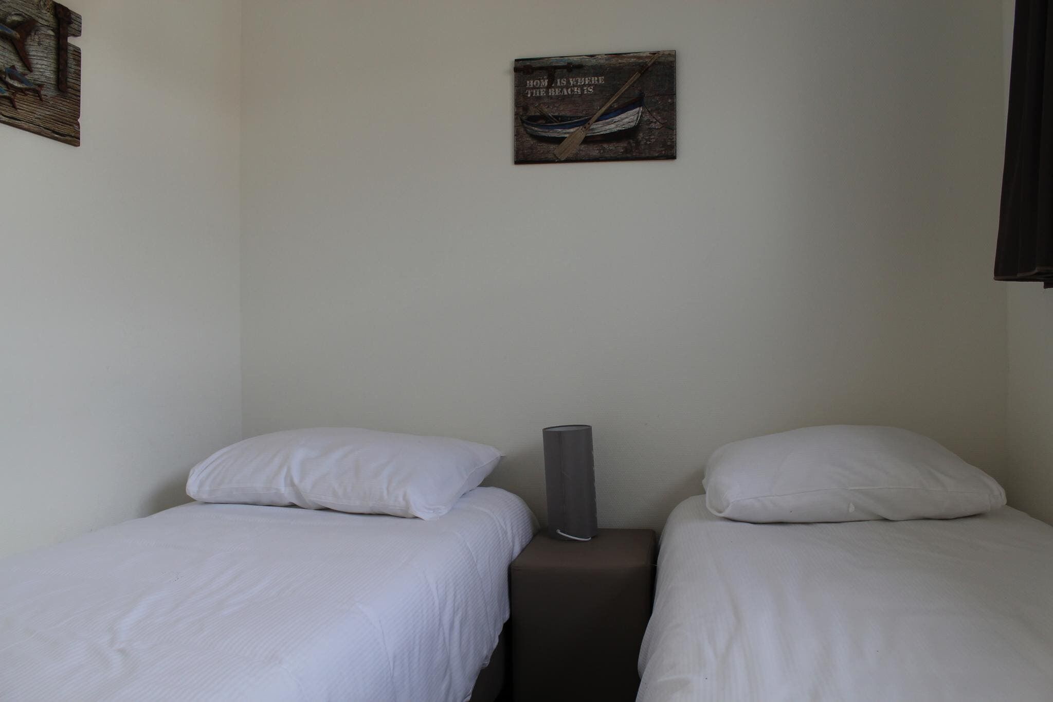 A small, simple room with two single beds, a nightstand with a lamp, and a wall-mounted picture.