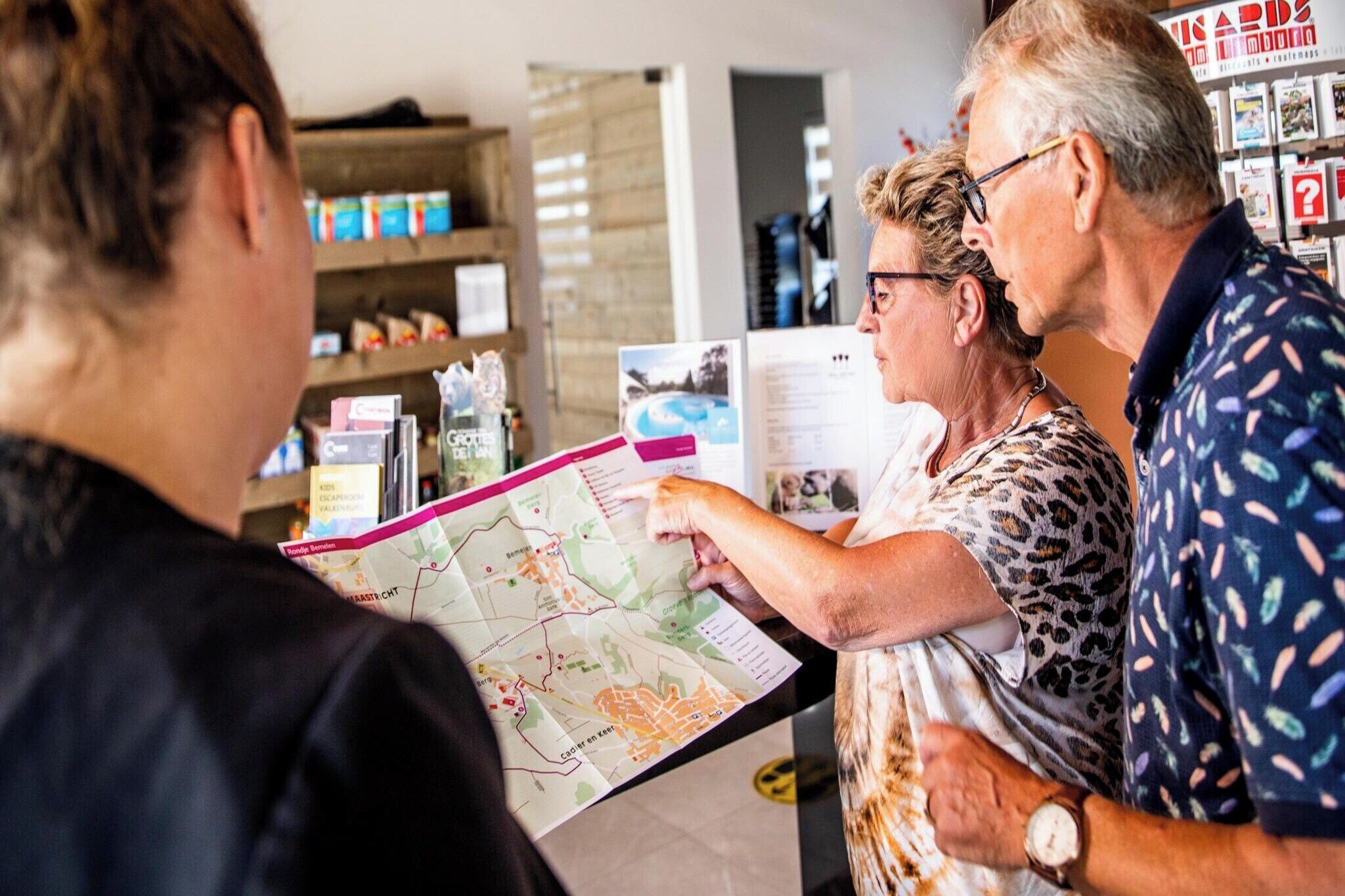 A group of people examining a map in a room with shelves containing various items.