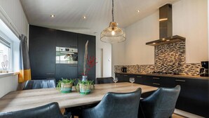 A modern kitchen with a black and white backsplash, a wooden dining table with chairs, and a hanging light fixture.