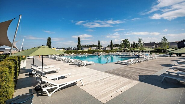 A pool area with lounge chairs and umbrellas, surrounded by greenery and buildings.