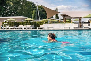 Une piscine entourée de verdure, avec des chaises longues et des parasols.