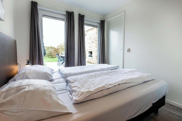A bedroom with a bed, curtains, and a view of the outdoors.
