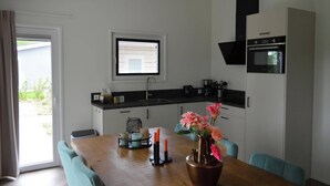 A modern kitchen with a black countertop, white cabinets, and a built-in oven. There is a dining table with chairs and a window with blinds.