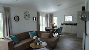 A modern living room with a sofa, coffee table, and a dining area with chairs and a TV.