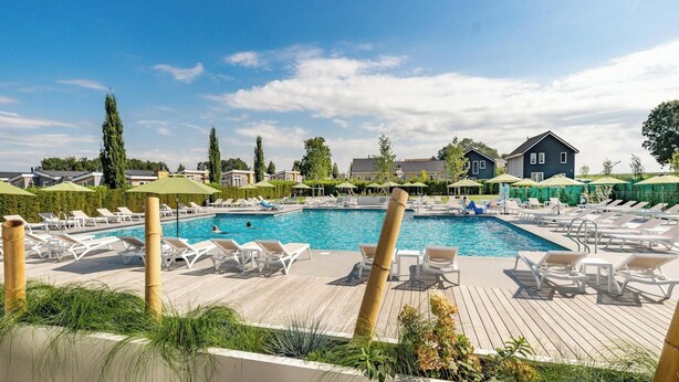 A swimming pool with lounge chairs and umbrellas, surrounded by houses and greenery.