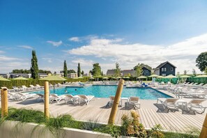Une piscine entourée de maisons et de verdure, avec des chaises longues et des parasols.