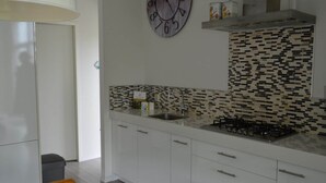 Een moderne keuken met witte kastjes, een zwart-wit betegelde achterwand, een gasfornuis en een klok aan de muur.