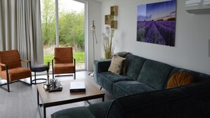 Een moderne woonkamer met een groene bank, twee fauteuils, een salontafel en een groot raam met uitzicht op groen.