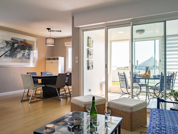 A modern living room with a dining area, a glass table with wine glasses, and a view of the outside.