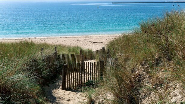 A beach with a wooden fence leading to the shore, clear blue water, and a distant ship. - Entre port et plages by Interhome (Audierne)