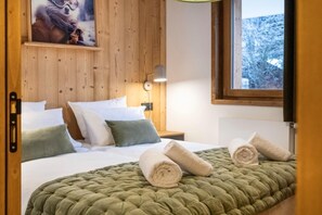 Et hotelværelse med sengegavl i træ, grøn quiltet dyne og et vindue med udsigt til sneklædte træer.
