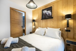 Une chambre avec un lambris en bois, un lit avec une literie blanche, deux lampes de chevet et un tableau encadré au-dessus du lit.