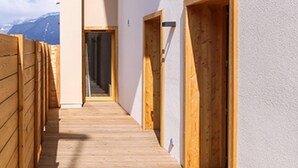 Een houten gang met deuren naar kamers, een witte muur en een uitzicht op bergen op de achtergrond.